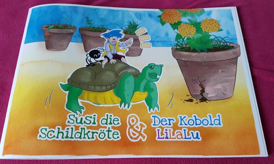 Cover des Susi-Buchs, es zeigt eine bunte Illustration der Schildkröte Susi und des blauhaarigen Kobolds LiLaLu, der auf ihr reitet, zusammen mit einer Spinne mit lachendem Gesicht.